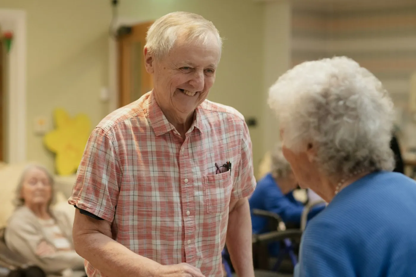 Zwei lächelnde Seniorinnen und Senioren im Gespräch im Gemeinschaftsraum